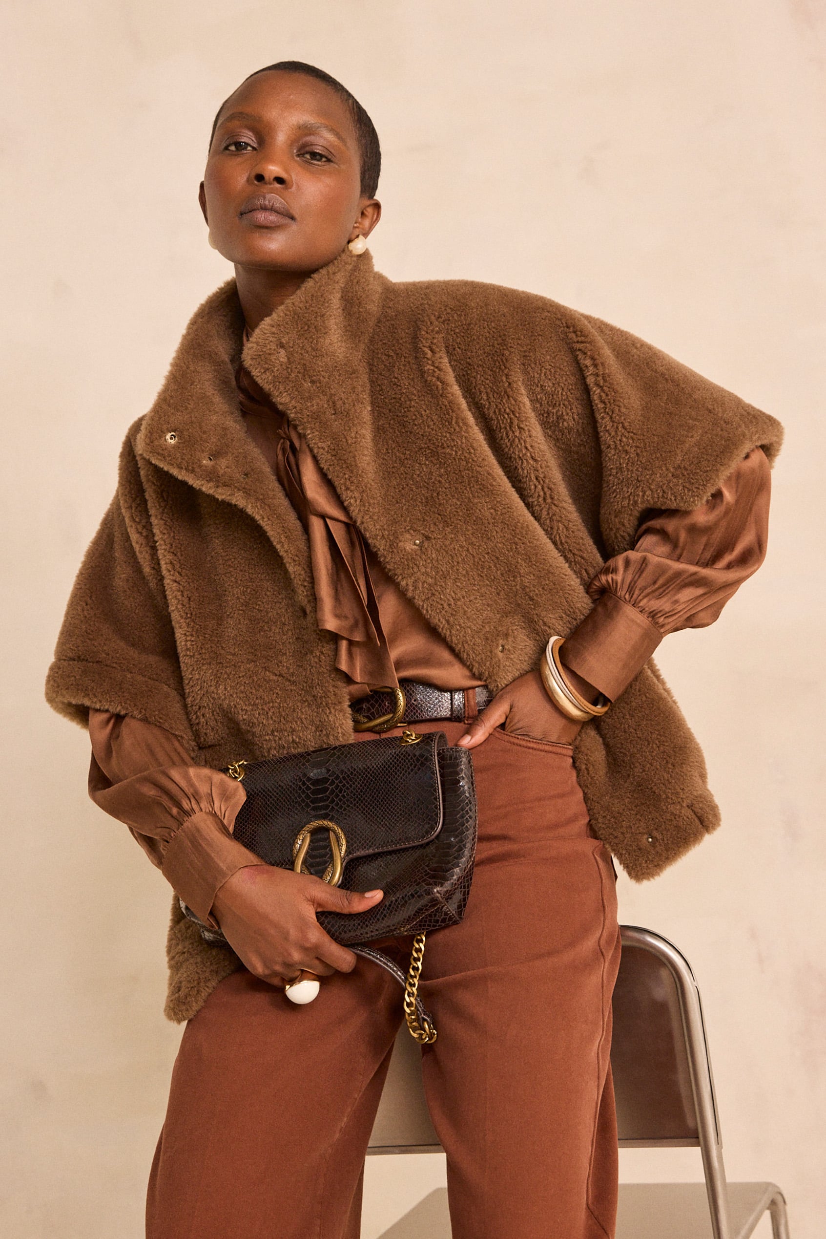 Femme portant une veste en fausse fourrure marron et un pantalon rouille, sac noir à la main
